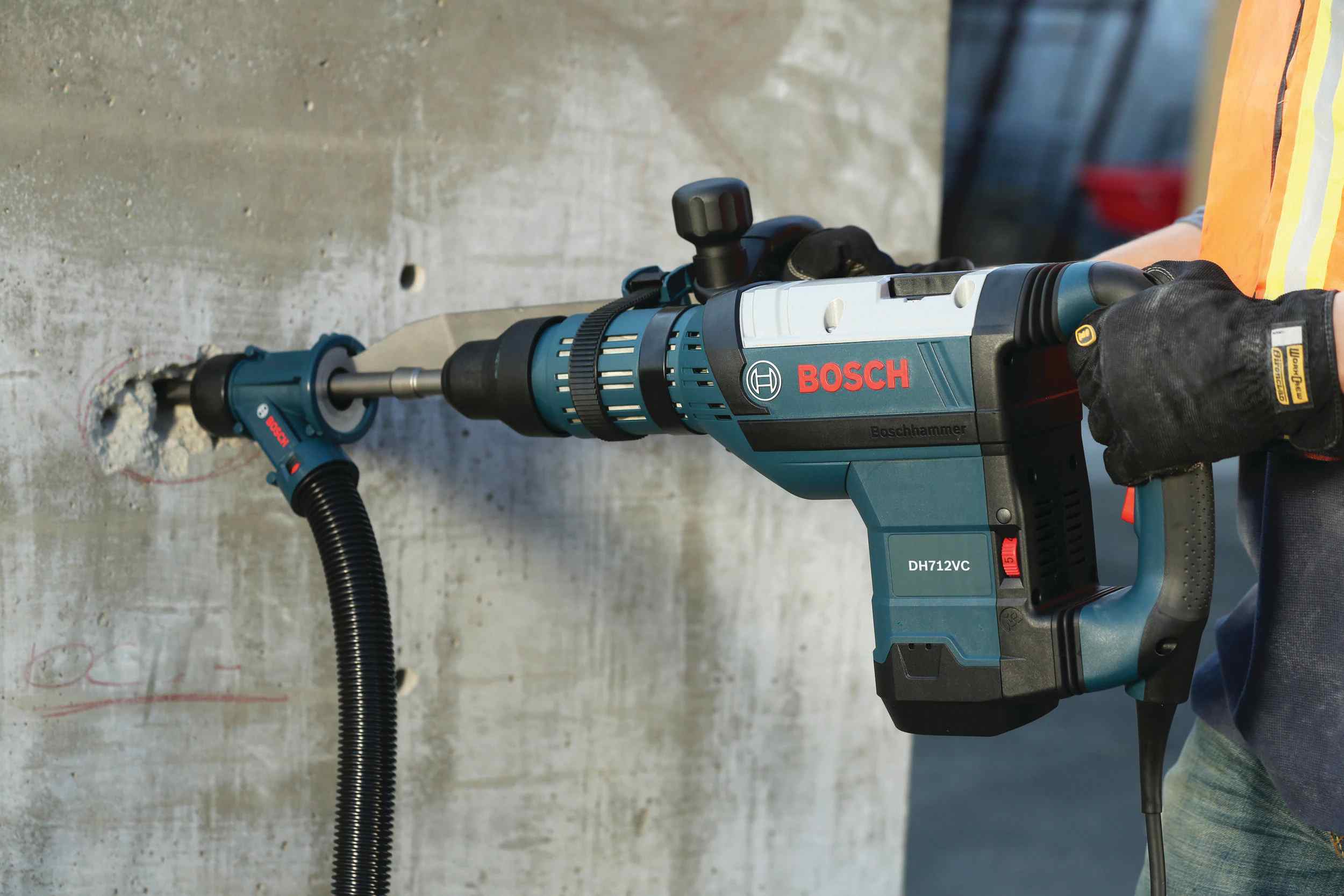 Close-up of a professional using a Bosch rotary hammer with a dust extraction attachment and the HS1936 SDS-Max R-Tec chisel bit to break into a solid concrete wall.