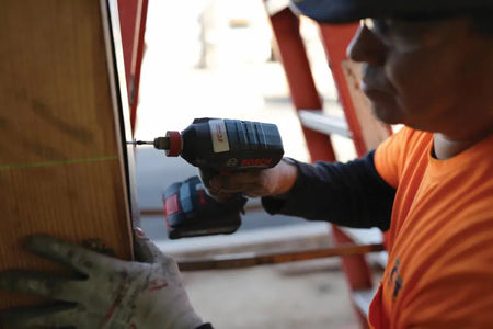 Close-up of the Bosch 18V "Freak" impact driver driving a fastener into a wooden stud, highlighting the precision provided by the variable speed trigger and brushless motor.