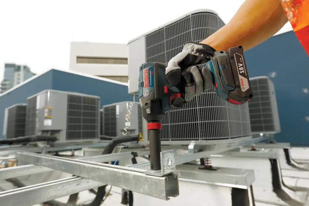 A technician using the Bosch 18V "Freak" impact driver with a deep-well socket on the 1/2-inch square drive to secure mounting brackets for heavy industrial HVAC units on a rooftop.