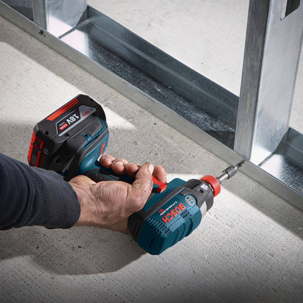 Close-up action shot of a worker using the impact driver and bit to drive a self-tapping screw into a metal track on a concrete floor.