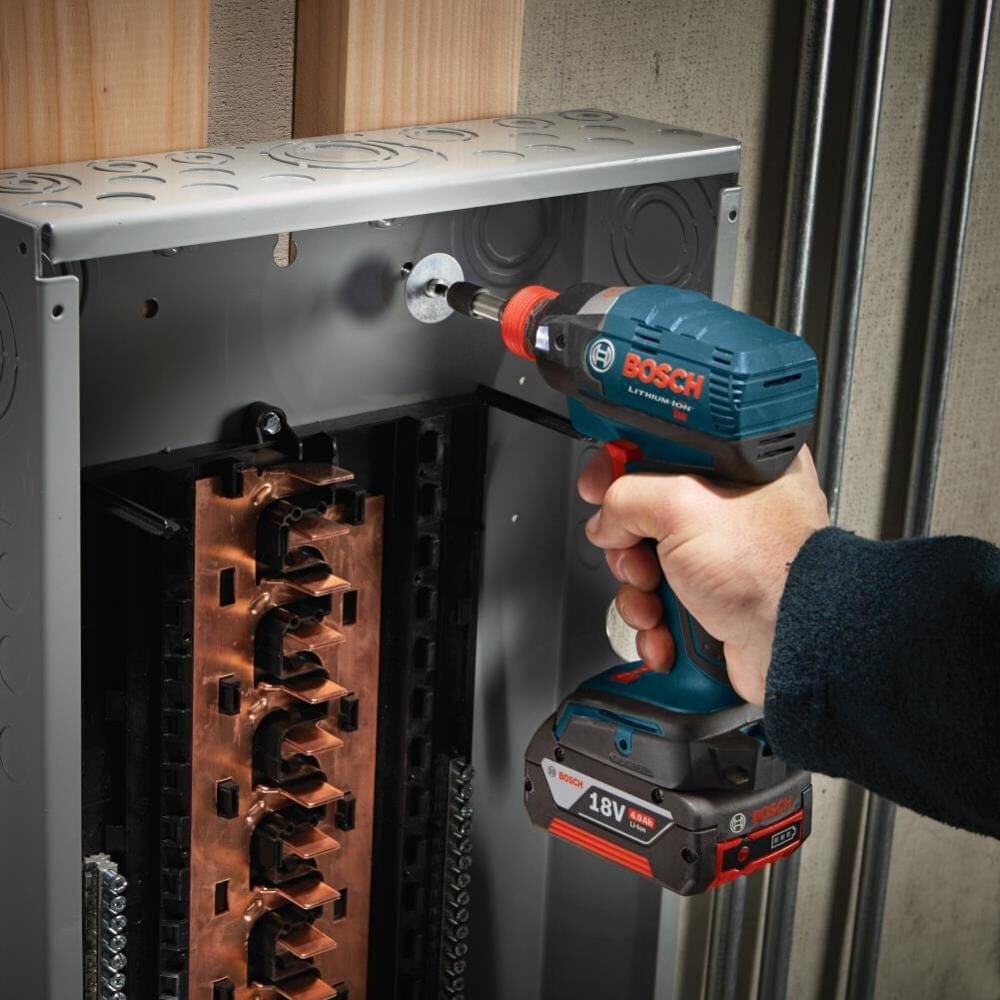 Action shot of an electrician using the impact driver and bit to secure a component inside a metal electrical service box.