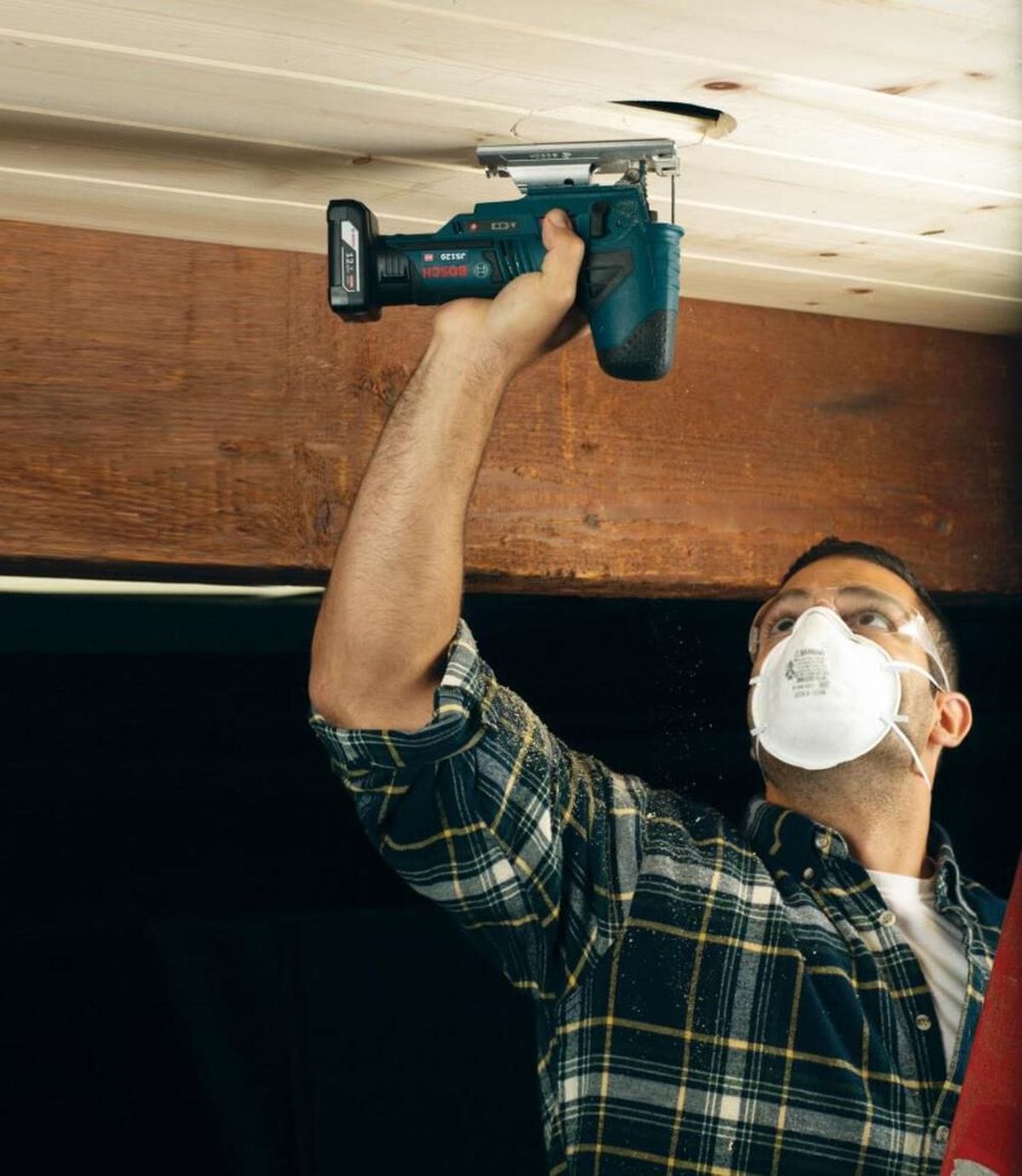 An action photo of a contractor using the Bosch JS120N-RT 12V Max jig saw to perform an overhead cut in a ceiling panel, illustrating the tool's lightweight design and balance for awkward positions.