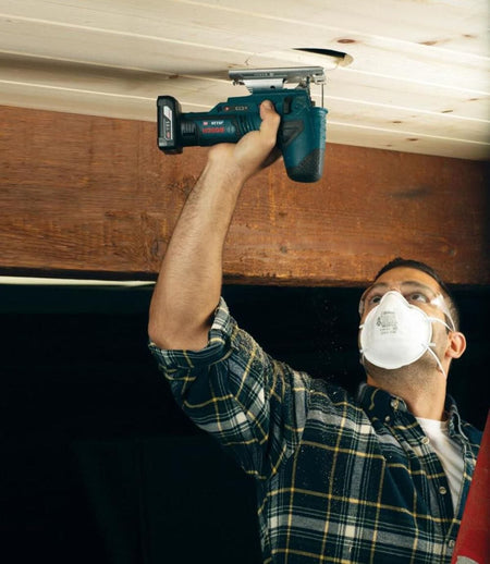 An action photo of a contractor using the Bosch JS120N-RT 12V Max jig saw to perform an overhead cut in a ceiling panel, illustrating the tool's lightweight design and balance for awkward positions.