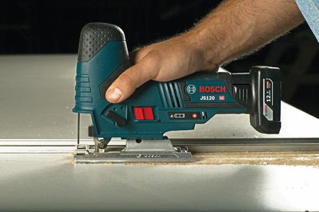 A contractor utilizing the Bosch cordless jig saw alongside a guide rail on a flat workpiece, demonstrating the stability of the die-cast aluminum footplate for straight, clean cuts.