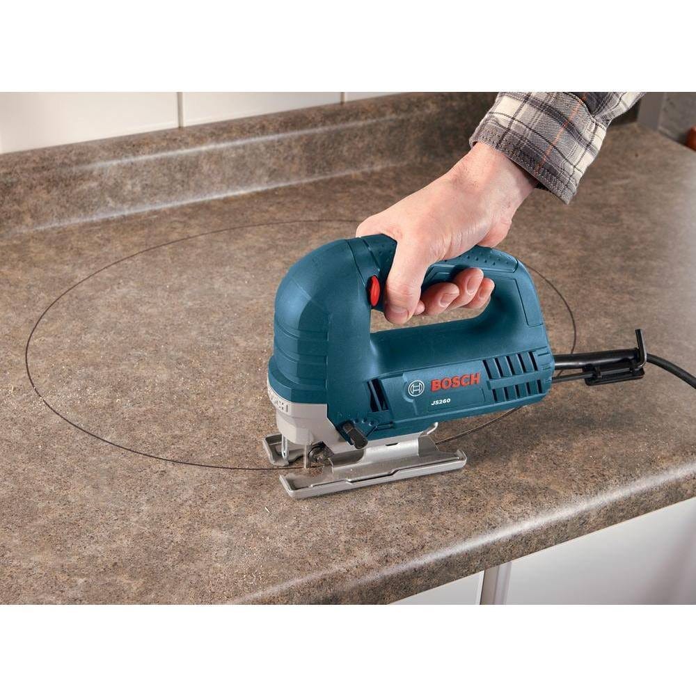 Person using Bosch jigsaw to cut circular shape into countertop; tool guided along marked line with one hand.