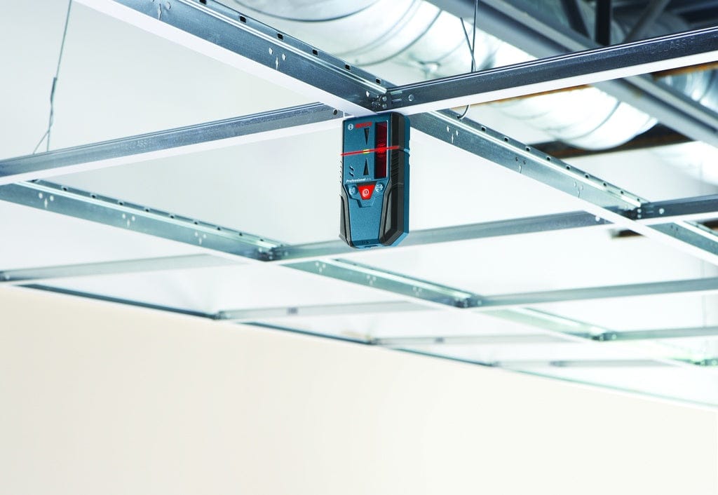 A Bosch LR6 red-beam line laser receiver magnetically attached to a metal ceiling grid, showing the horizontal laser line crossing the center on-grade indicator.