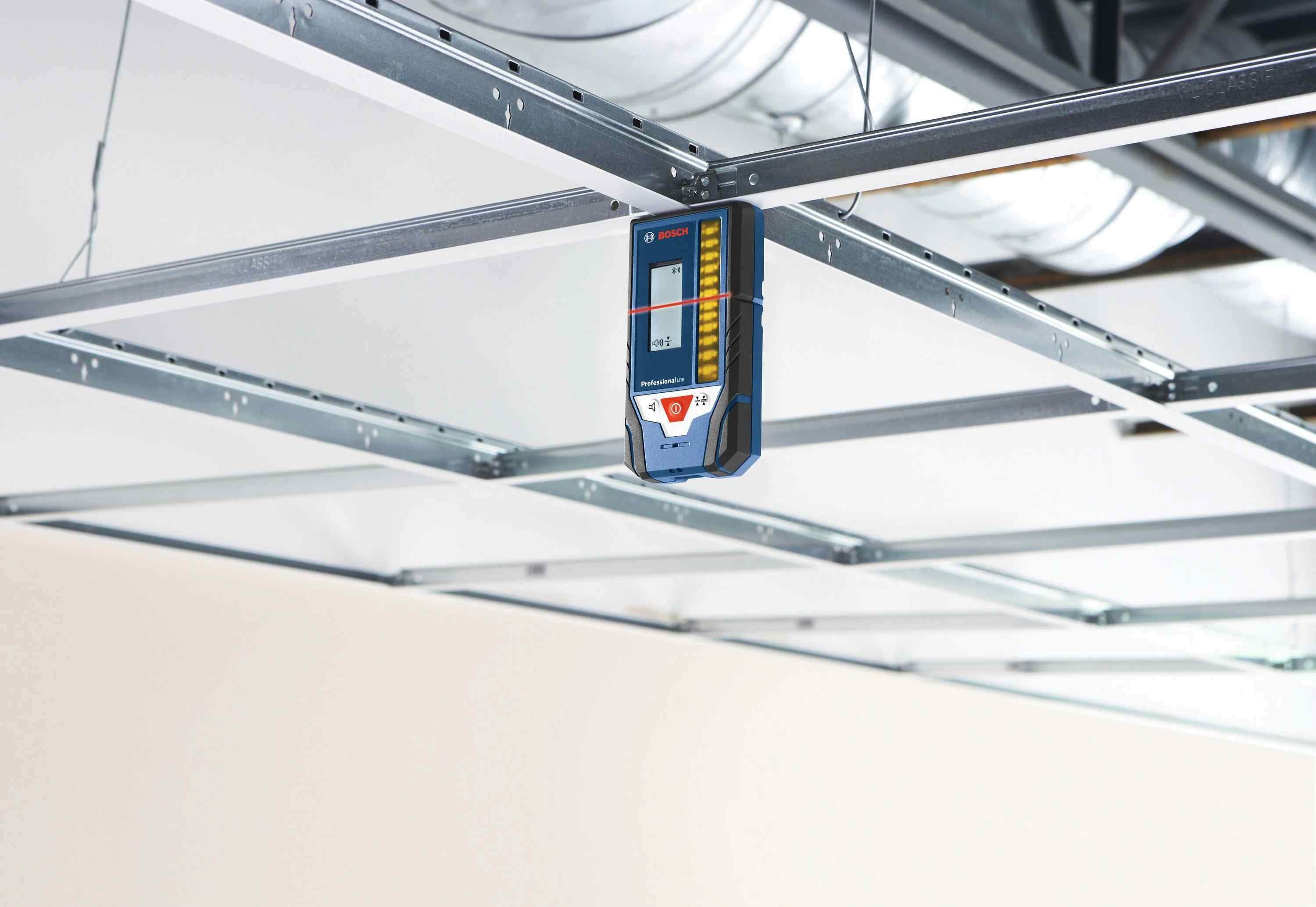 A Bosch LR8 line laser receiver magnetically attached to a metal ceiling grid on an interior jobsite, catching a red laser beam for precise suspended ceiling installation.