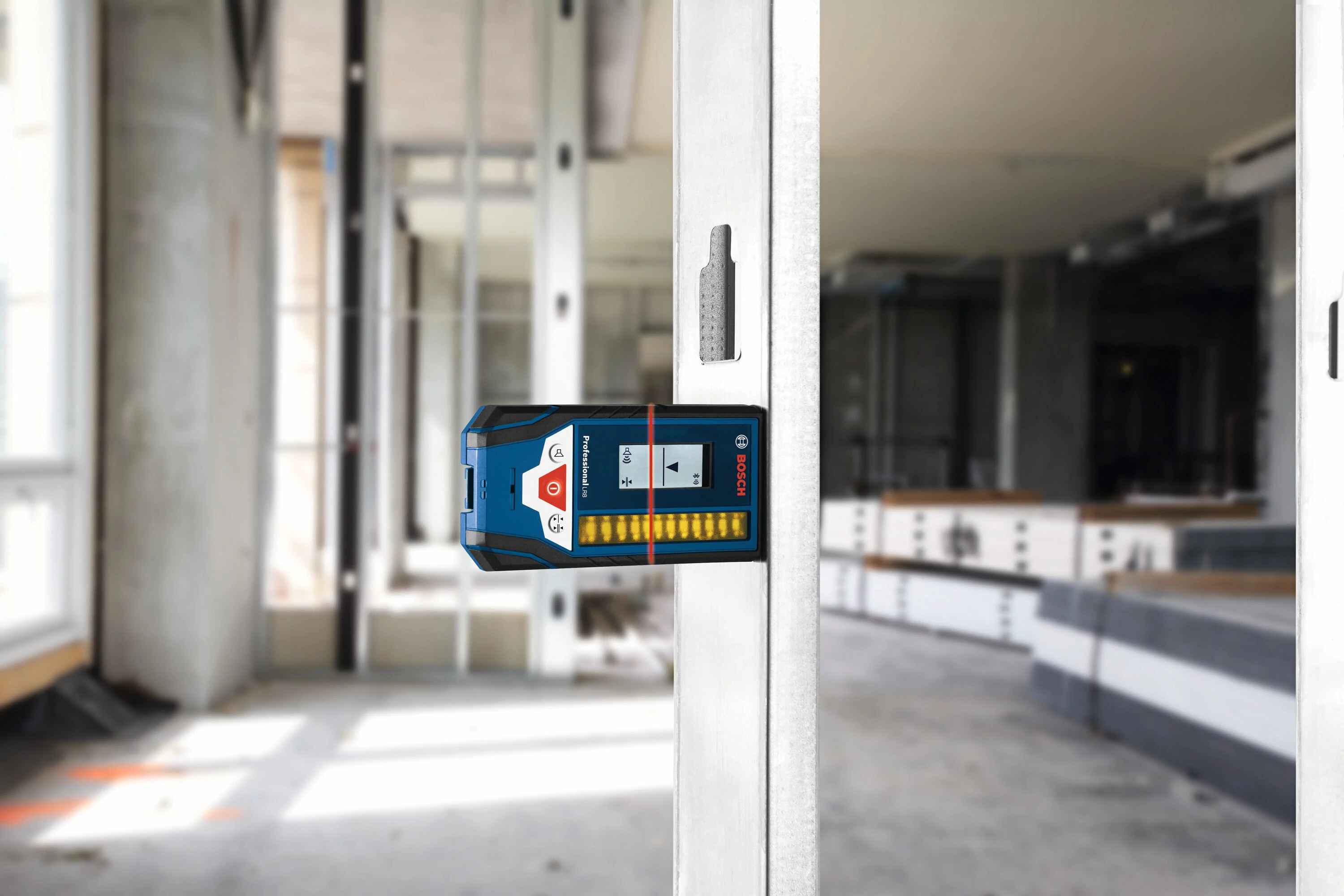 A professional using the Bosch LR8 digital detector magnetically mounted to a metal wall stud to verify the exact height of a red laser line in a commercial construction setting.