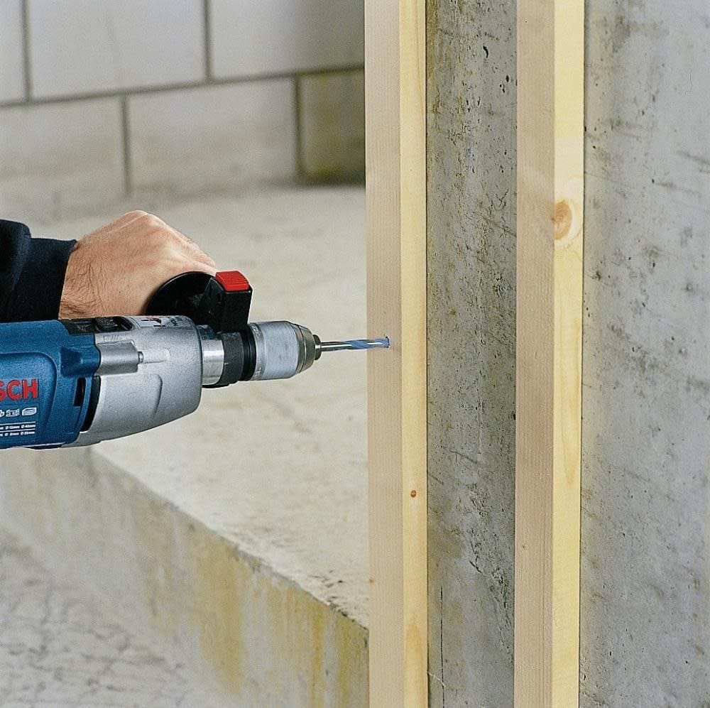 Action shot of a worker using a Bosch drill equipped with the Multi-Construction bit to drill through a wooden stud directly into a concrete wall.