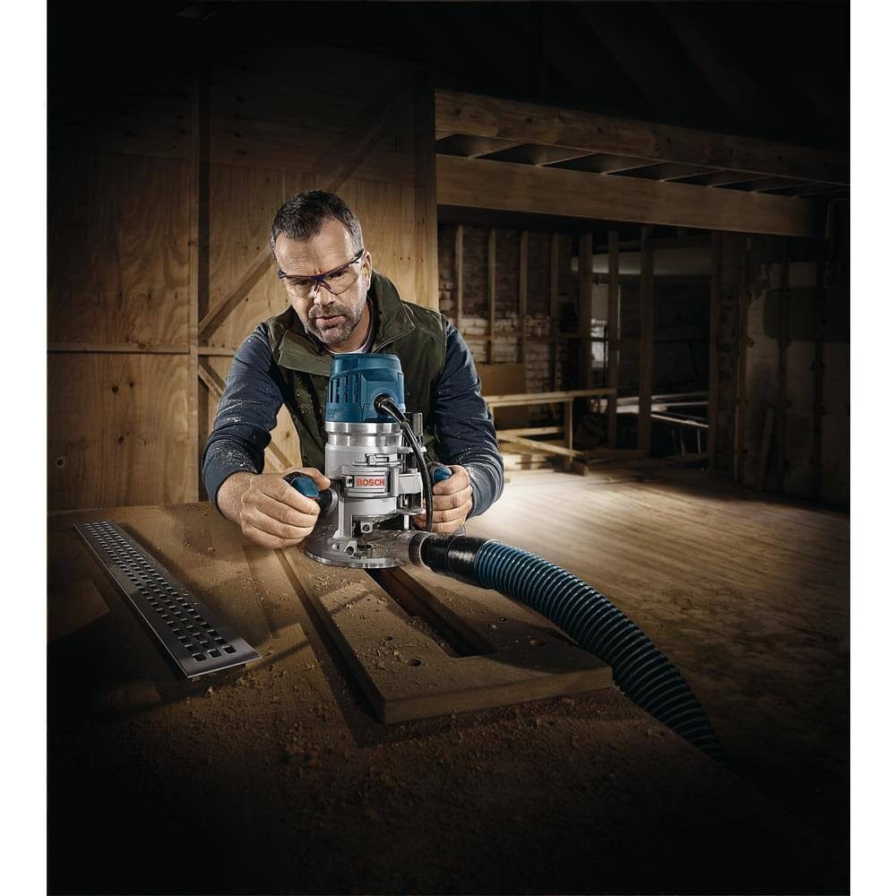 Person using Bosch router with dust extraction hose in woodworking environment; safety glasses worn during operation.