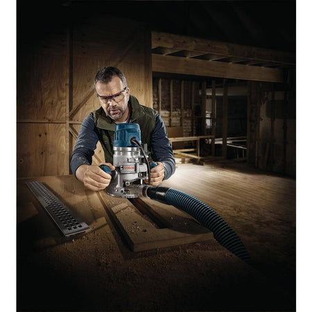 Person using Bosch router with dust extraction hose in woodworking environment; safety glasses worn during operation.