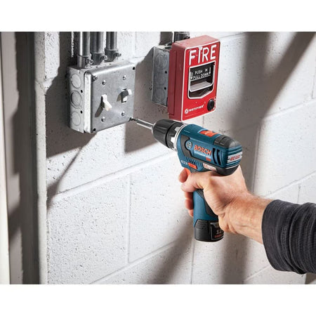 An electrician using a cordless drill and a driver bit from the Bosch MS4034 34-piece set to perform maintenance on a light switch box in a commercial or industrial setting.