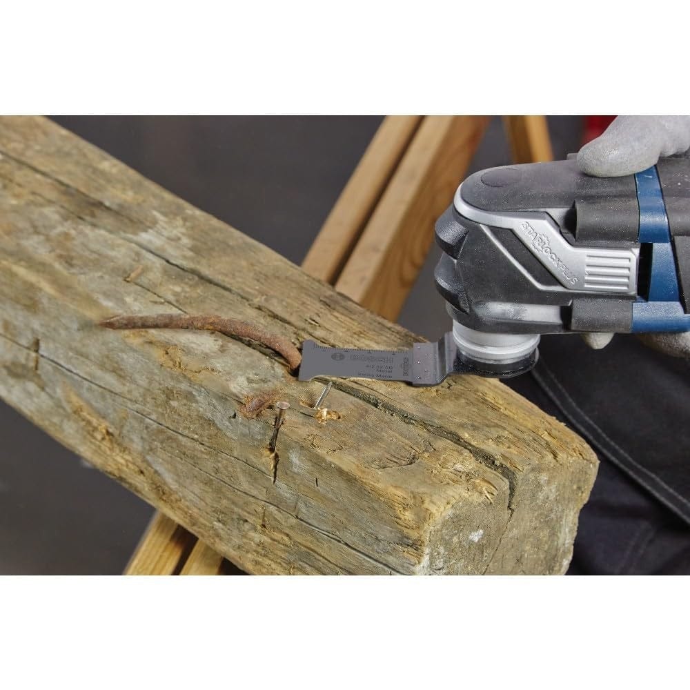 A wide-angle action photograph showing a professional using a Bosch oscillating multi-tool with the OSL034C carbide blade to perform a precise plunge cut through heavy-duty metal fasteners in old lumber.