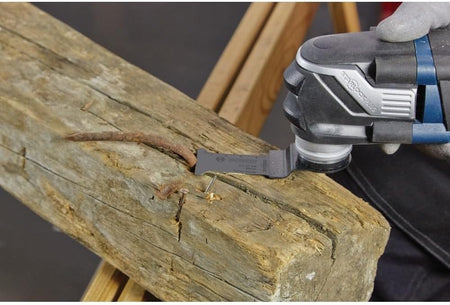 Close-up action shot of the carbide plunge cut blade slicing through a rusted nail embedded in a thick wooden beam.