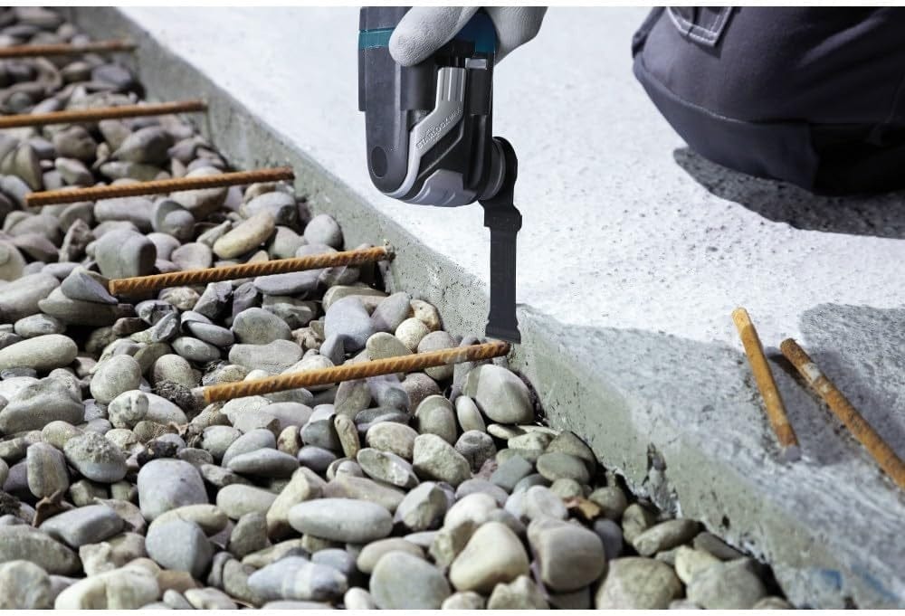Action shot of the blade cutting through metal rebar on the ground near a concrete slab and gravel.