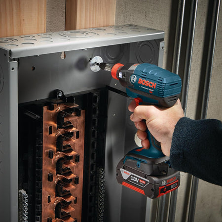 A close-up electrical application photograph showing a technician using a Bosch 18V impact driver and a long Impact Tough Phillips #2 screwdriver bit to fasten ground screws inside a grey metallic electrical service panel box.