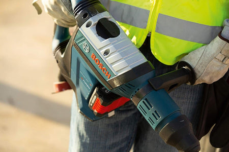 Close-up view of a worker's hands holding the Bosch GBH18V-45CK24 PROFACTOR 18V Hitman rotary hammer, highlighting the top-mounted Vario-Lock mode selector dial and heavy-duty tool construction.