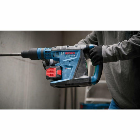Bosch GBH18V-45C rotary hammer drill used horizontally on masonry surface. Tool features BITURBO Brushless label. Worker wears gloves and long sleeves in industrial setting.