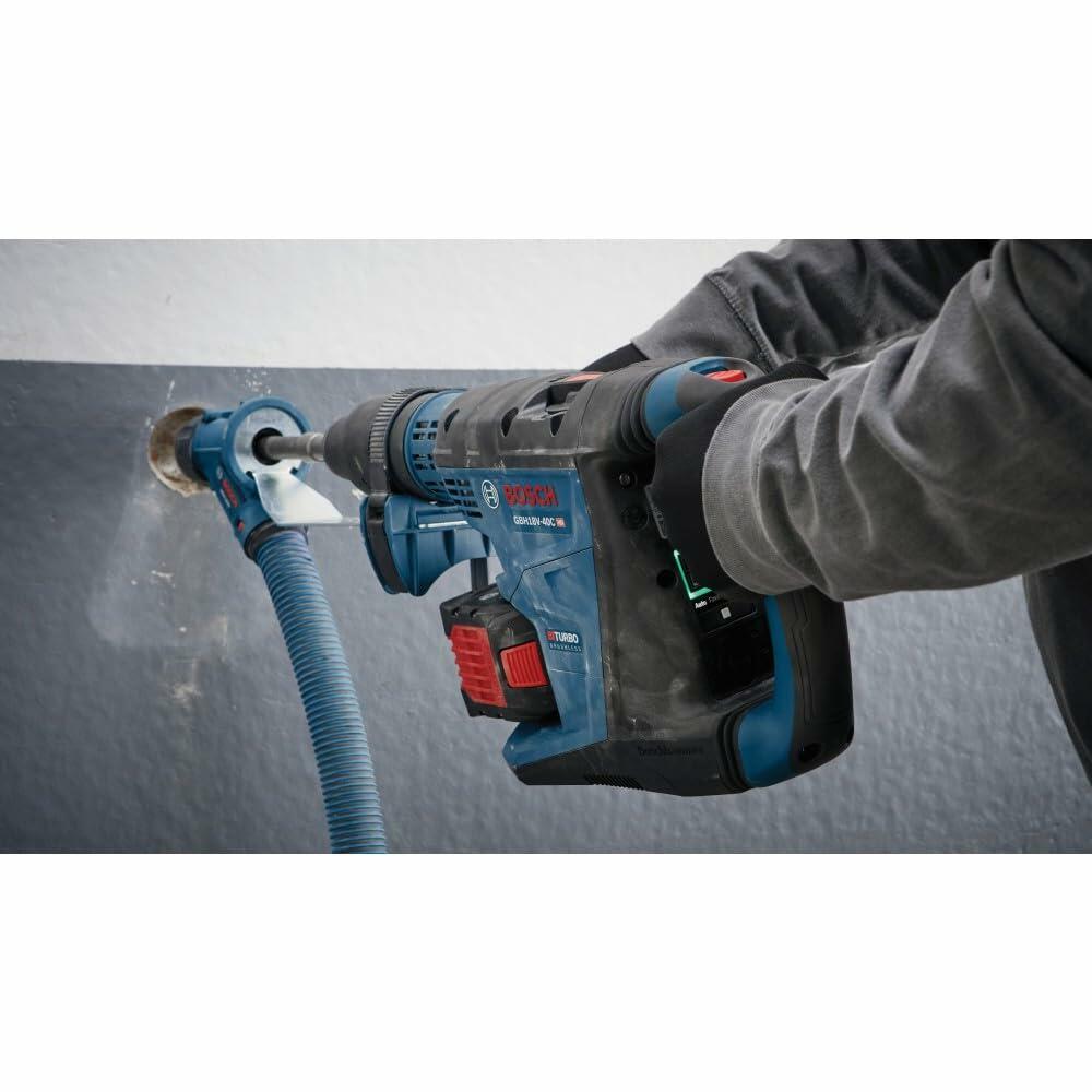 Bosch GBH18V-26 rotary hammer drill in use with dust extraction attachment. Worker drills into concrete wall while wearing gloves. Hose system minimizes airborne dust during operation.