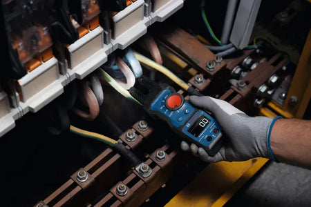 An industrial electrician wearing protective gear using the integrated LED flashlight on the Bosch PRO GFM1000-15 open jaw multi tester. The bright light cleanly illuminates a dark mechanical control terminal array to ensure safe, precise diagnostic troubleshooting on complex non linear loads.