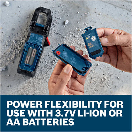 A close up overhead view of an open battery compartment cover being held next to the back of the Bosch PRO GMC 600-15 Clamp Meter tool. The lower marketing text reads Power flexibility for use with 3.7V Li-Ion or AA batteries, illustrating its versatile power options and built in protective safety cutoff.