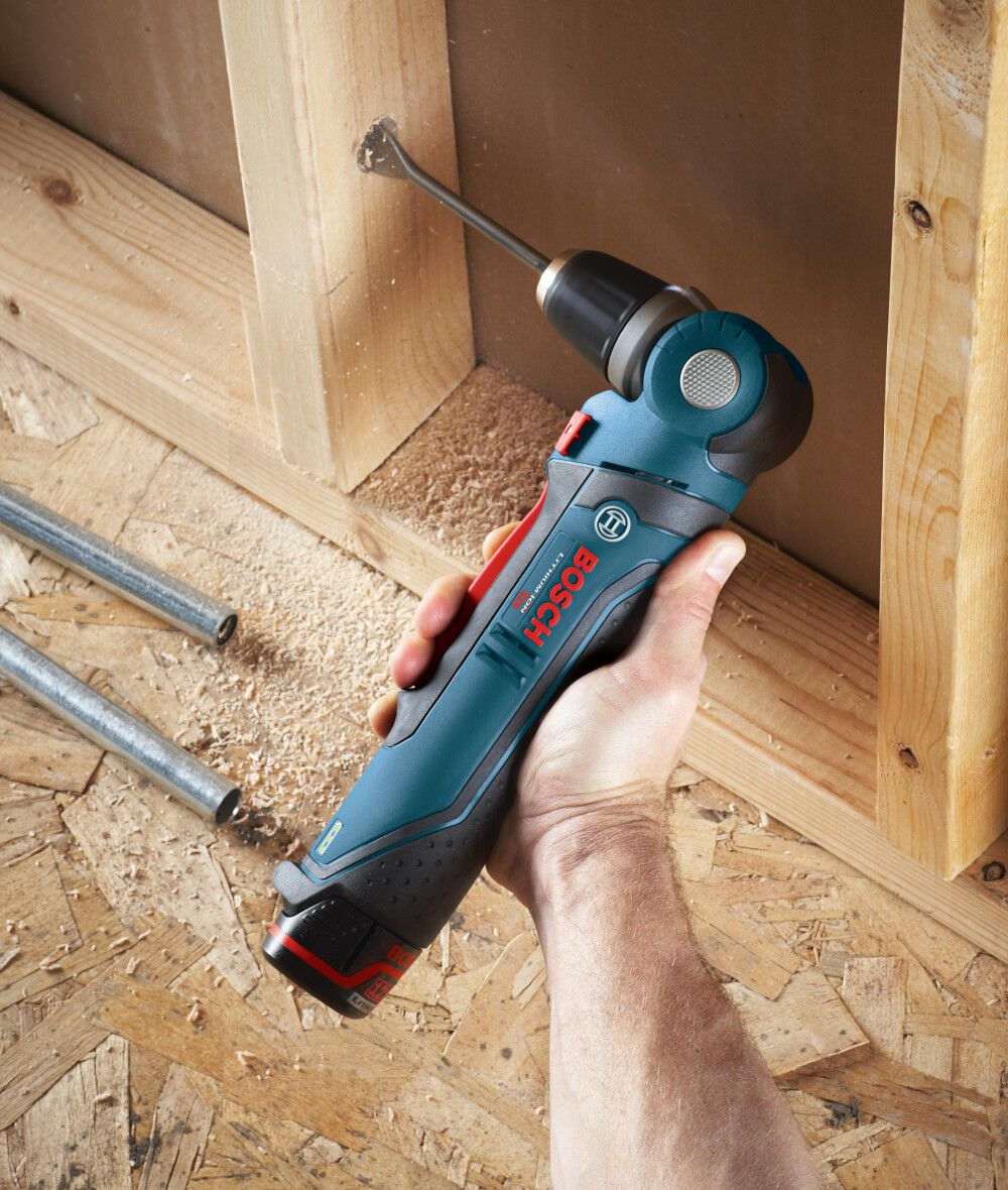 Action shot of a user holding the Bosch right angle drill to bore a hole through a wooden wall stud using a spade bit, highlighting the tool's compact size and ergonomic grip for residential construction tasks.