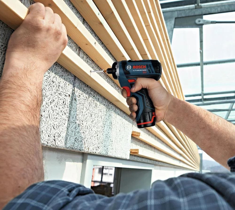 A contractor utilizing the lightweight Bosch cordless screwdriver to fasten screws into wooden wall slats in a well-lit construction environment.