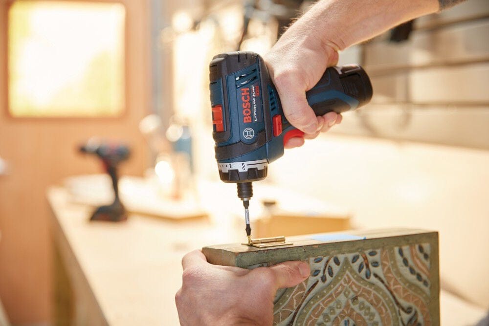 Action shot focusing on a woodworker using the 12V Max pocket driver to precisely drive a screw into a light-colored wooden workpiece on a workbench.