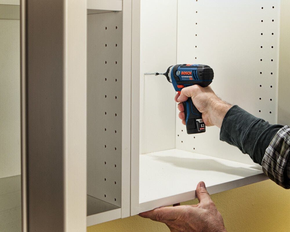 Action shot showing a professional using the Bosch pocket driver to fasten a screw inside a white cabinet, demonstrating the tool's compact size and maneuverability in tight quarters.