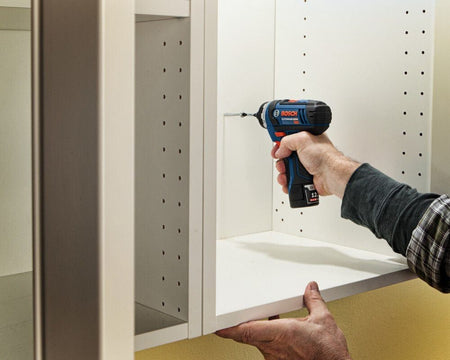 Action shot showing a professional using the Bosch pocket driver to fasten a screw inside a white cabinet, demonstrating the tool's compact size and maneuverability in tight quarters.