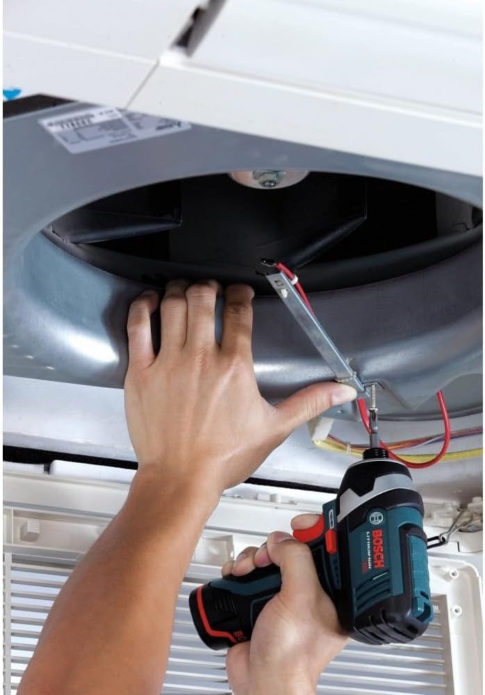 A close-up of a person using the Bosch PS41-2A impact driver overhead to drive a screw into the metal housing of a ceiling vent system.
