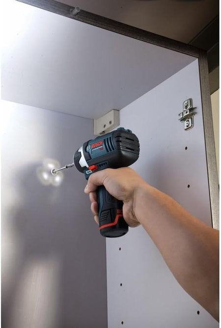 A person using the Bosch PS41-2A impact driver inside a white cabinet, showing how the integrated LED light ring illuminates the dark corner while driving a screw.