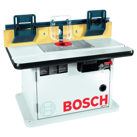 An e-commerce studio product view of the white Bosch RA1171 benchtop cabinet style router table, showcasing the laminated work surface, precision aluminum insert plate with a red ring, tall fence with adjustable MDF faceplates, two blue featherboards, and a clear safety guard.