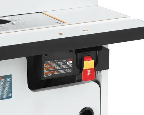 A close-up profile view of the front right corner of the router table, highlighting the laminated top plate, accessory slot, and the master electrical safety power switch with its prominent red paddle and yellow lock-out key.