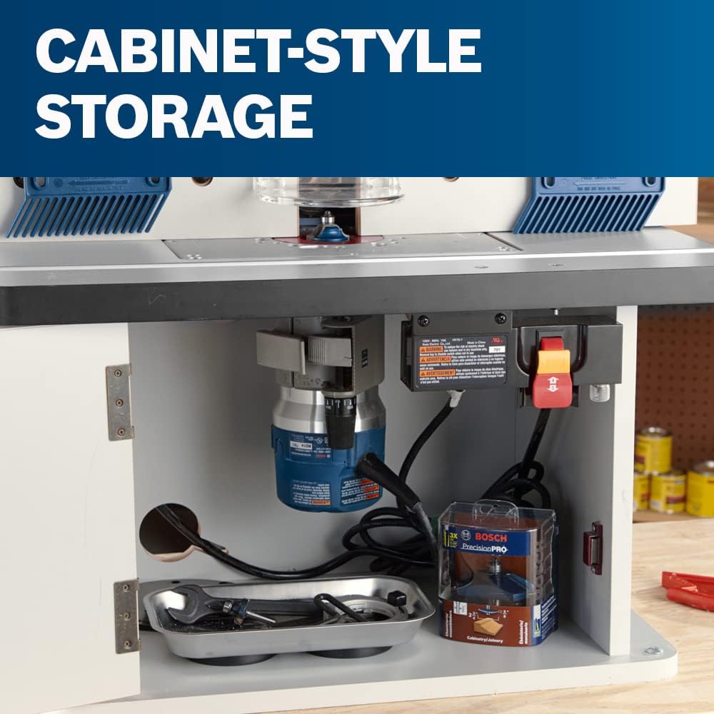An interior view of the open cabinet-style router table storage compartment, showing a blue Bosch router motor mounted beneath the table, a metal tool tray with a wrench, a packaged router bit, and a power safety switch module.