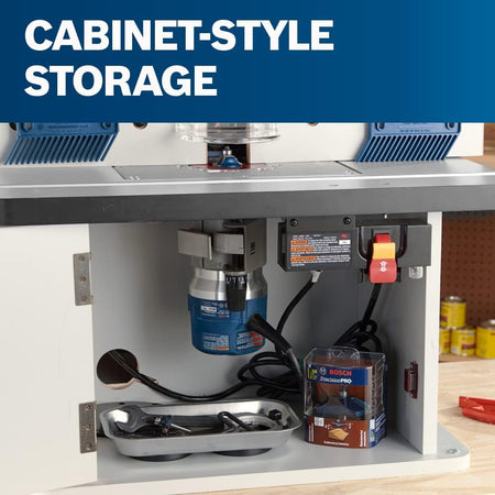 An interior view of the open cabinet-style router table storage compartment, showing a blue Bosch router motor mounted beneath the table, a metal tool tray with a wrench, a packaged router bit, and a power safety switch module.