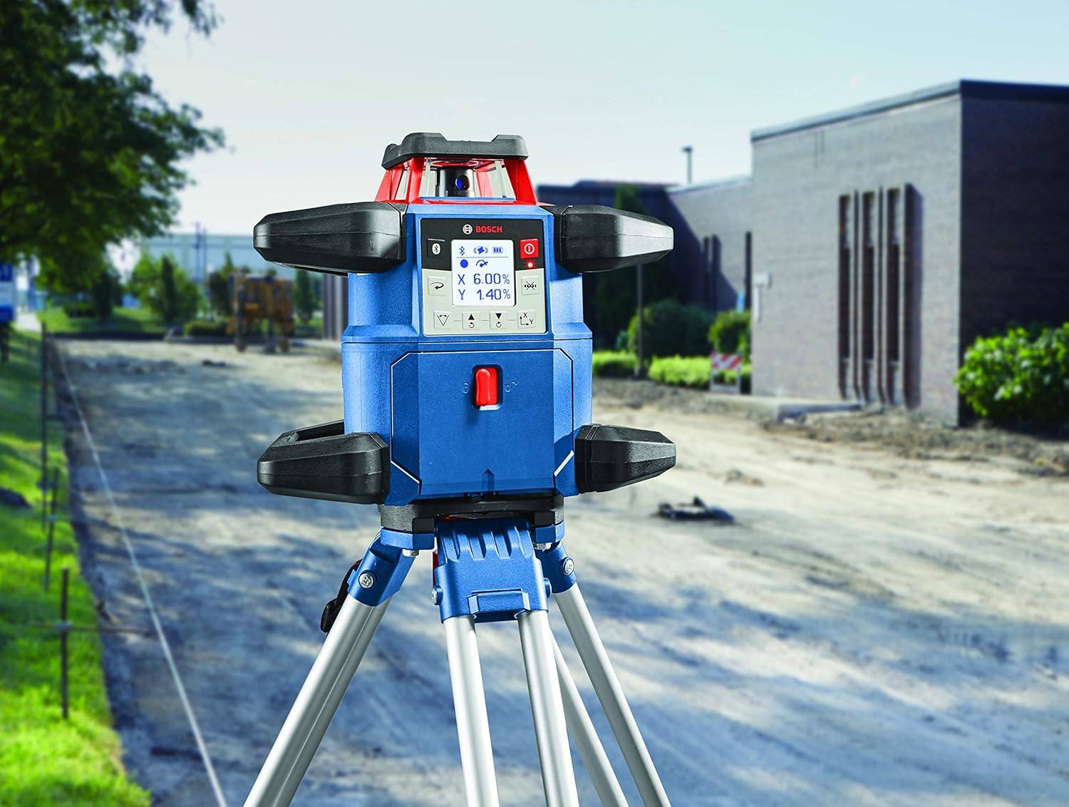 The Bosch REVOLVE4000 rotary laser level mounted on an aluminum tripod at a construction site, with the digital display showing the active slope percentages for site grading.