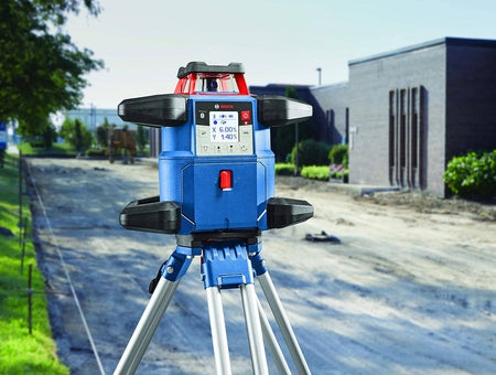 The Bosch REVOLVE4000 rotary laser level mounted on an aluminum tripod at a construction site, with the digital display showing the active slope percentages for site grading.