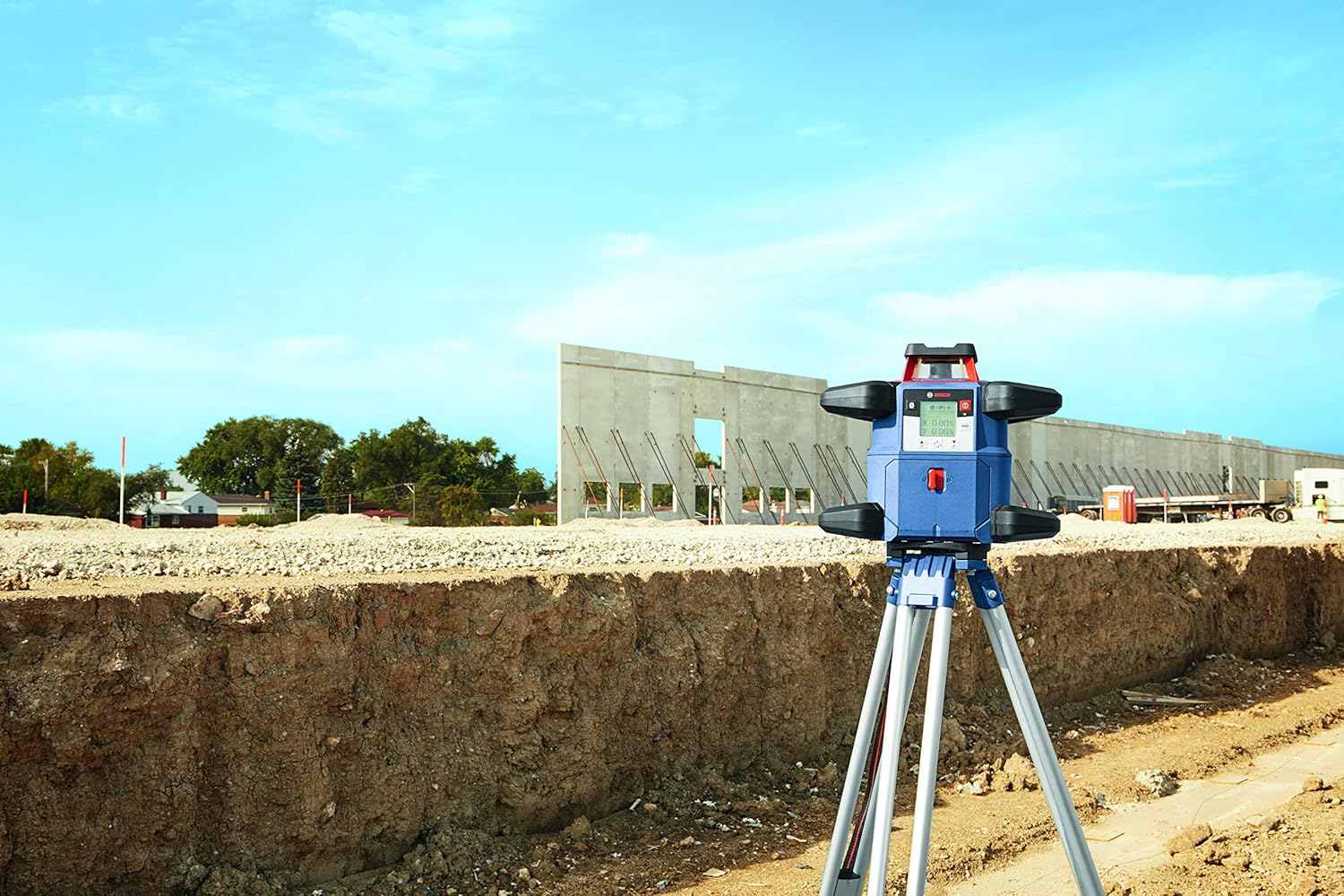 A construction site view of the Bosch GRL4000-80CH rotary laser mounted on a tripod in the foreground with large concrete retaining walls being built in the background.