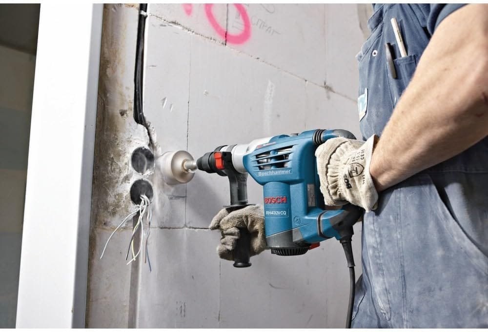 A close-up jobsite shot of a masonry technician using the Bosch 3-mode rotary hammer with a large carbide-tipped diamond hole saw core bit to bore a clean electrical outlet path through a reinforced white concrete wall.