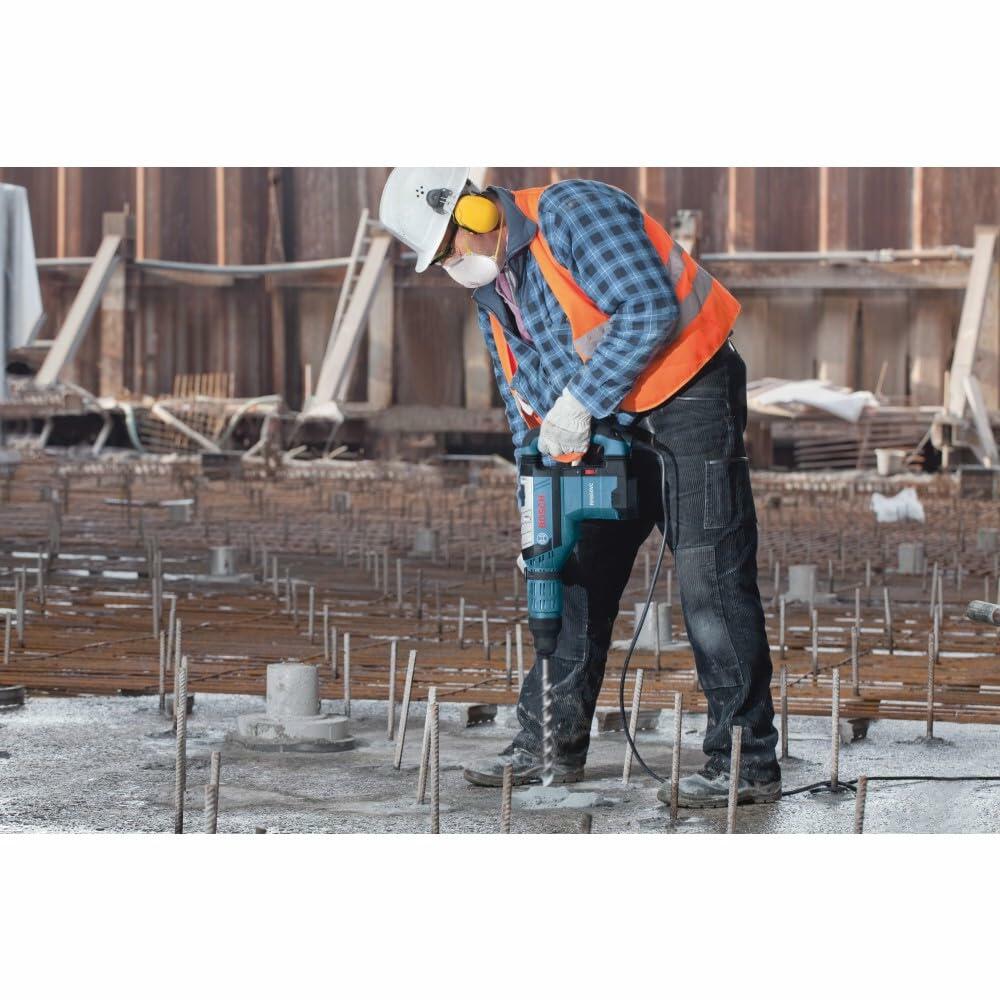A construction worker wearing safety gear uses the Bosch RH850VC hammer to drill vertically into a concrete foundation with exposed rebar.