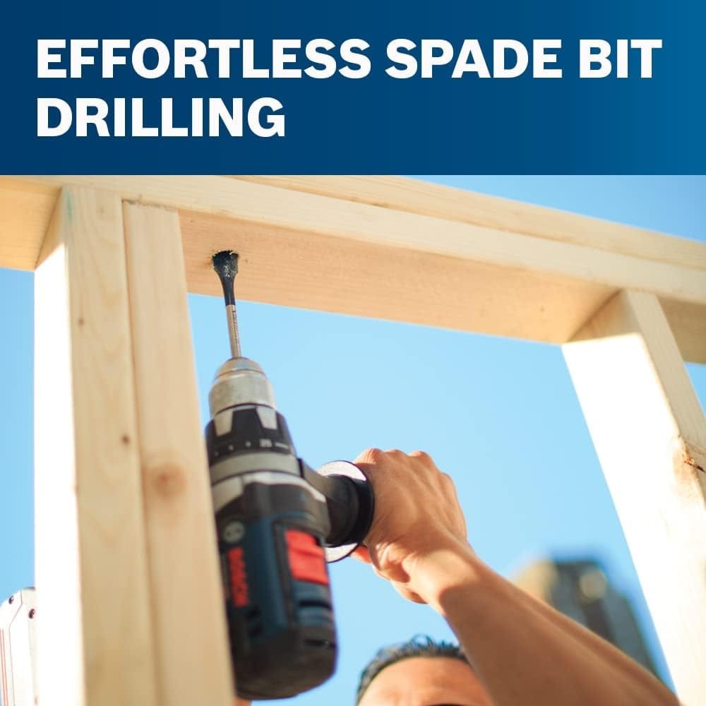 Low angle lifestyle shot of a construction worker using a drill with a spade bit to bore a hole through a wooden stud overhead.