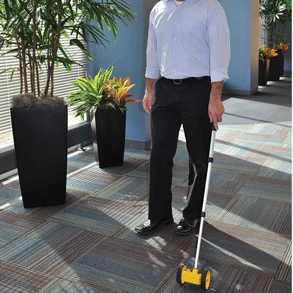 A person in business-casual attire uses the Bosch Rolatape RT204 measuring wheel to measure the carpeted floor of an office lobby.