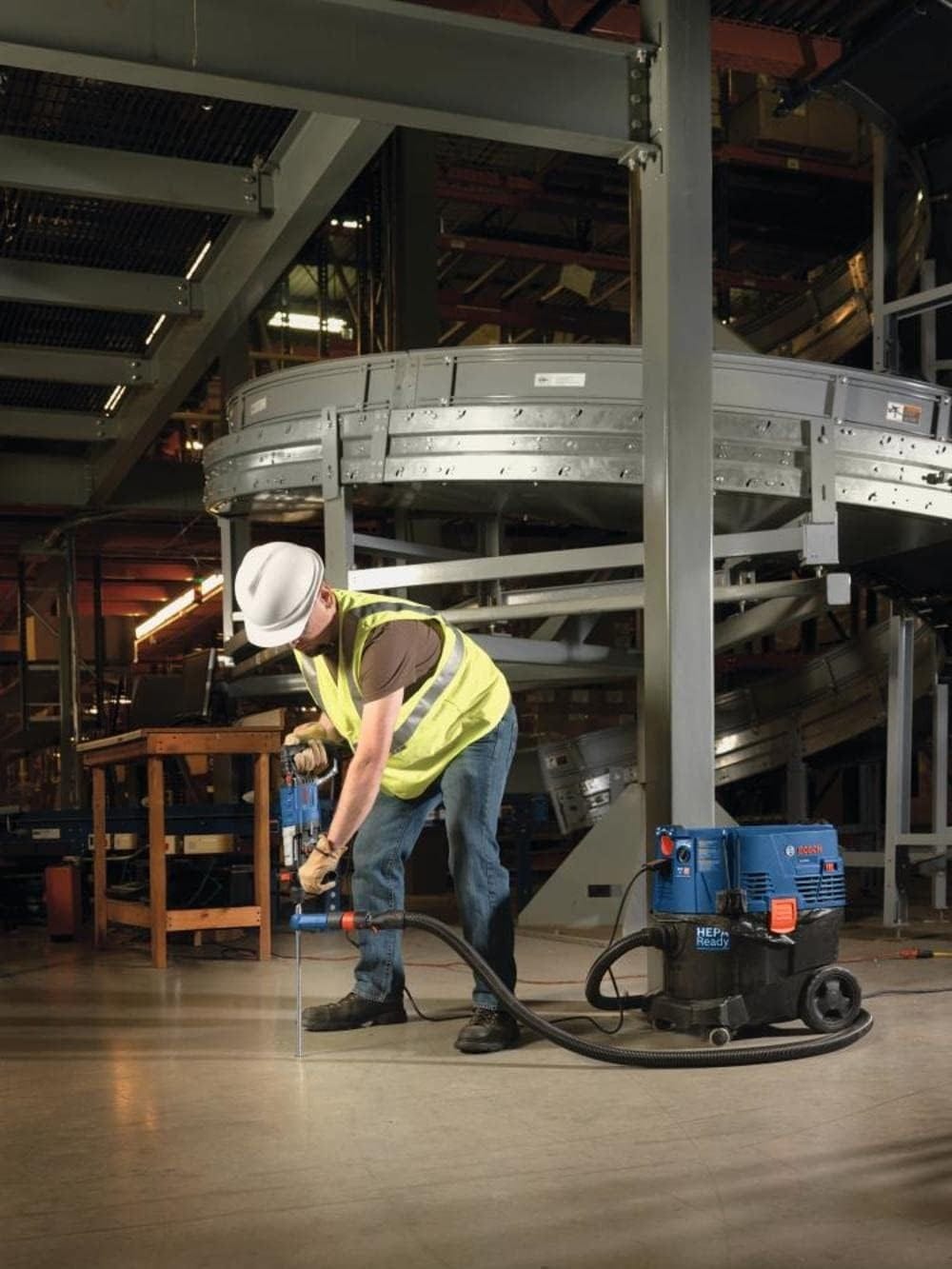 Action shot of a worker in a yellow vest using the Speed Clean bit to drill into a concrete floor in a warehouse setting.