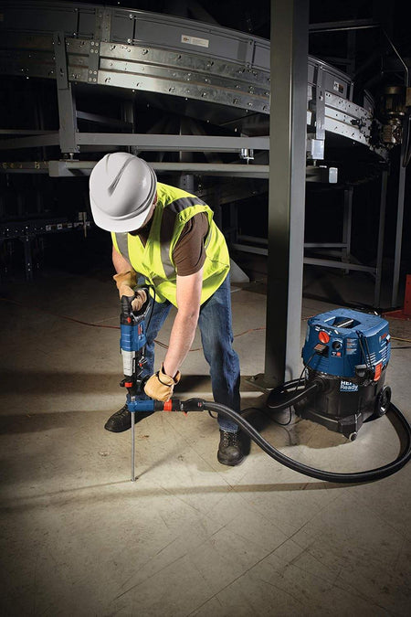 Action shot of a worker drilling into a concrete warehouse floor near industrial machinery using the dust extraction bit.
