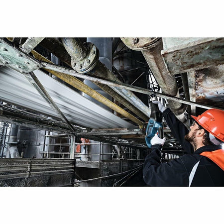 Worker in a red safety helmet using a Bosch reciprocating saw or impact tool on a large metal pipe in an industrial setting. The image highlights the tool’s utility in heavy-duty maintenance or construction environments.