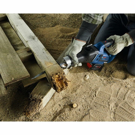 Person using a Bosch cordless reciprocating saw to cut through a damaged wooden beam outdoors. The user wears protective gloves and kneels on a sandy surface, demonstrating the saw’s portability and effectiveness in demolition or repair tasks