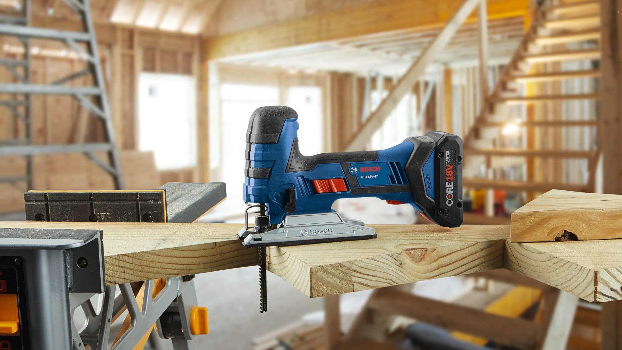 A blue Bosch cordless jigsaw resting on top of a wooden framing beam with a blade inserted in the tool holder.
