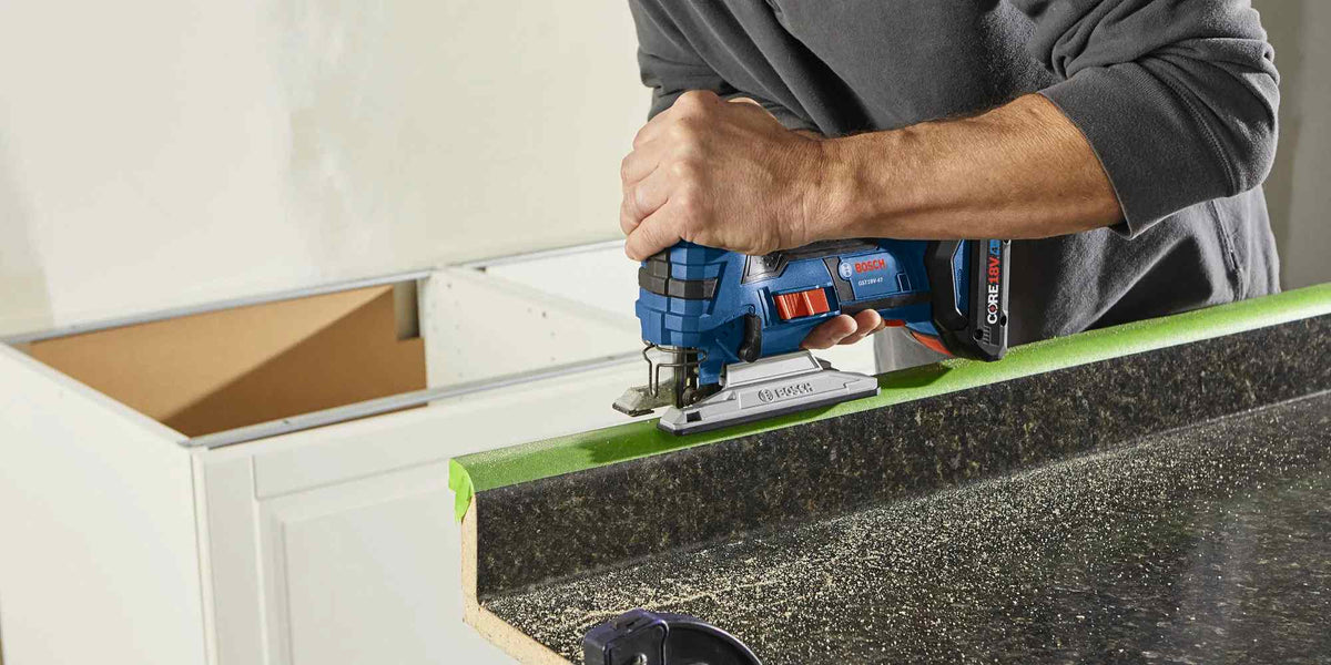 Action shot of a worker using a blue Bosch jigsaw to cut along the edge of a dark countertop surface.