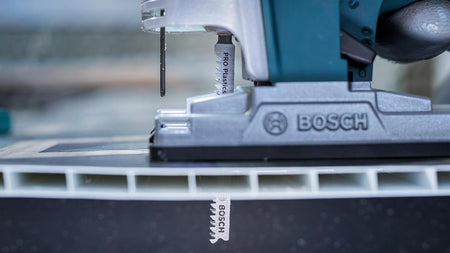 Side view of a Bosch jigsaw cutting through a white hollow PVC profile, highlighting the blade's clean cut through the material.